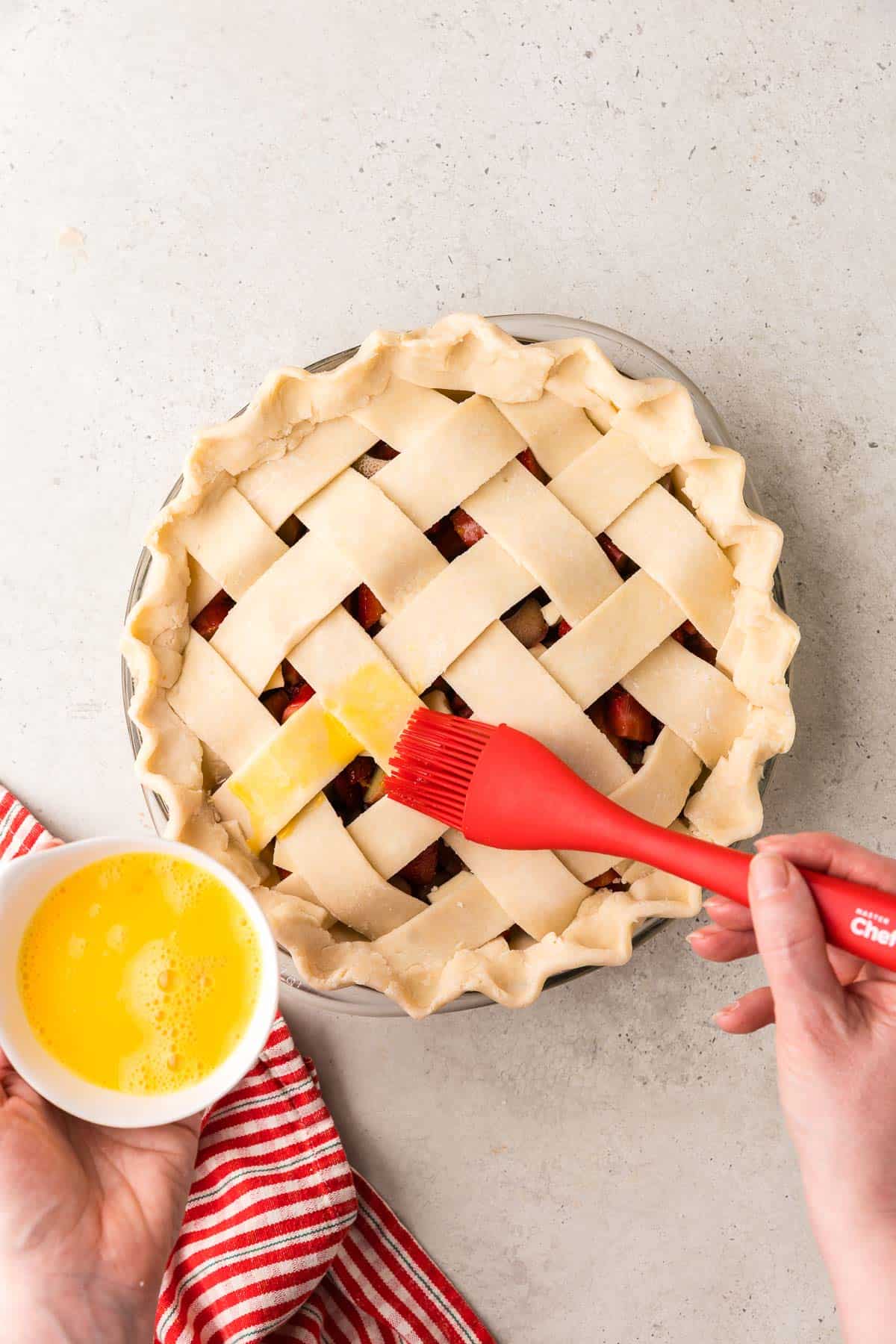 Overhead shot of a strawberry rhubarb pie with a lattice top having an egg wash brushed on.