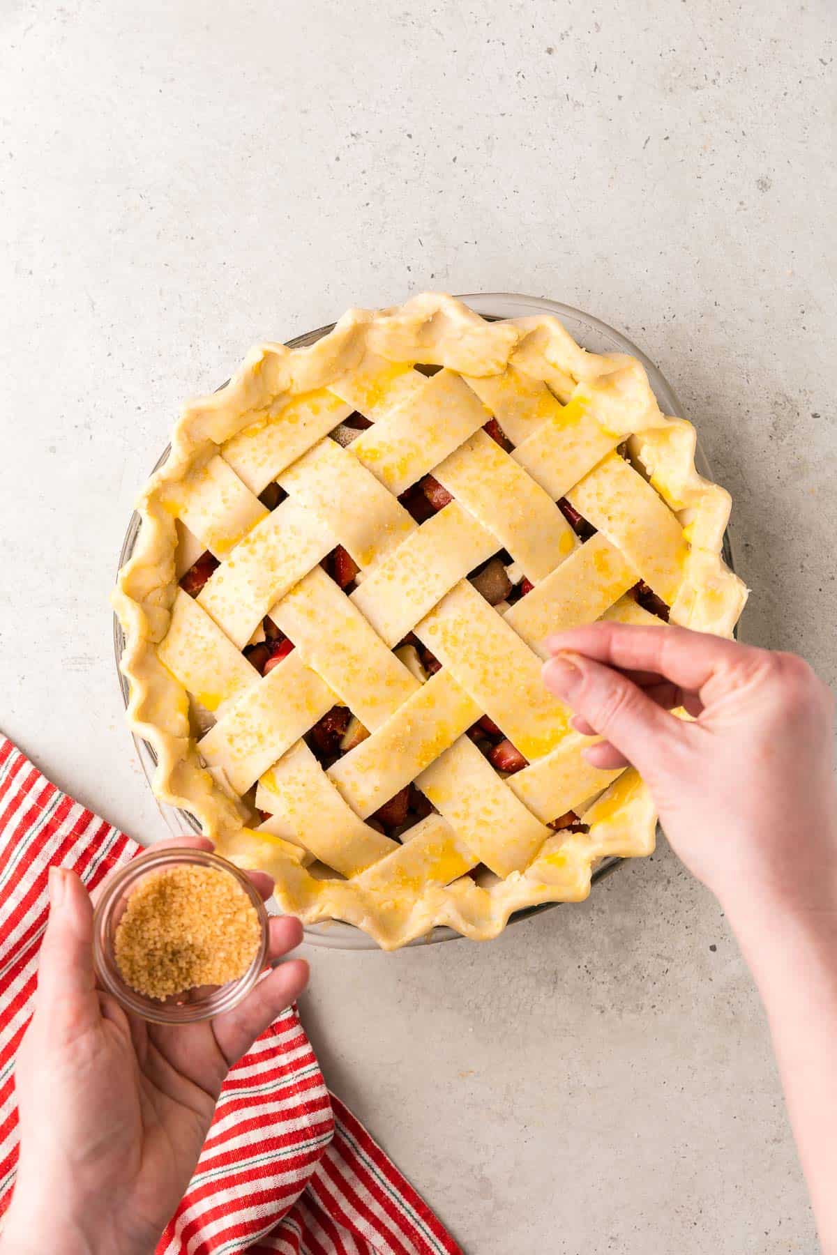 overhead shot of a strawberry rhubarb pie just before it goes in the oven. The lattice top has been brushed with egg wash and coarse sugar sprinkled on top.