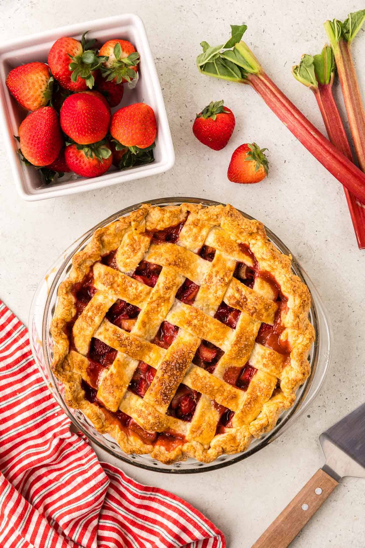 overhead shot of a strawberry rhubarb pie in a glass pie dish just after coming out of the oven. It has a lattice top and you can see the warm pink filling underneath.