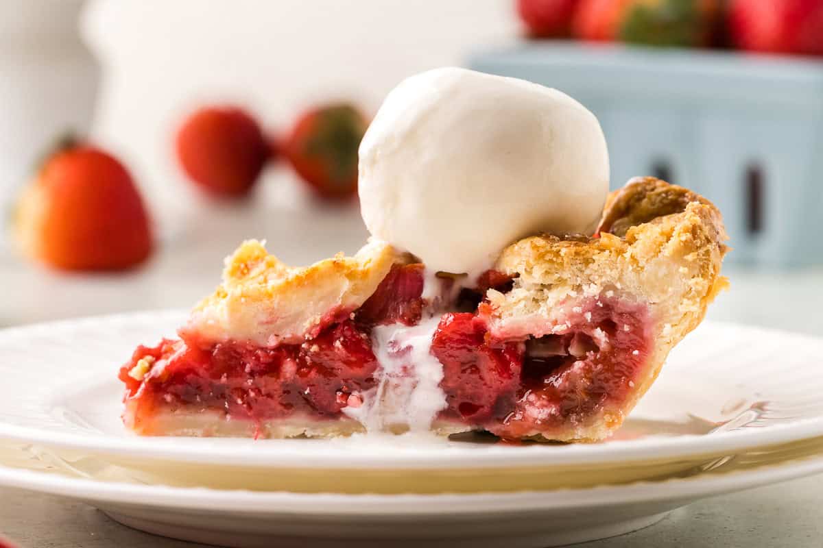 side shot of a slice of strawberry rhubarb pie with a scoop of vanilla ice cream melting on the top.