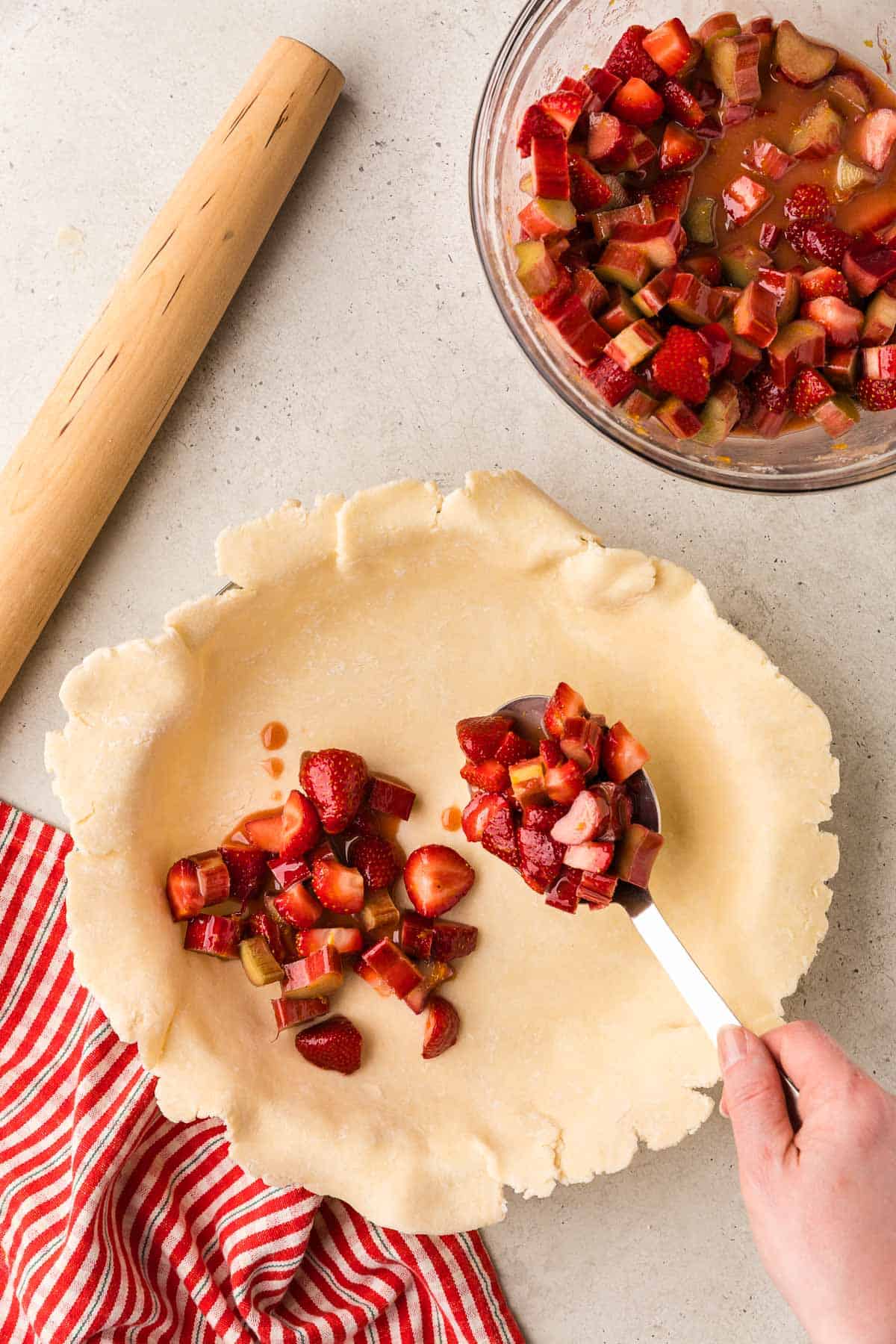 Overhead shot of the pie dough in the pie dish now being filled with the strawberry rhubarb pie filling.