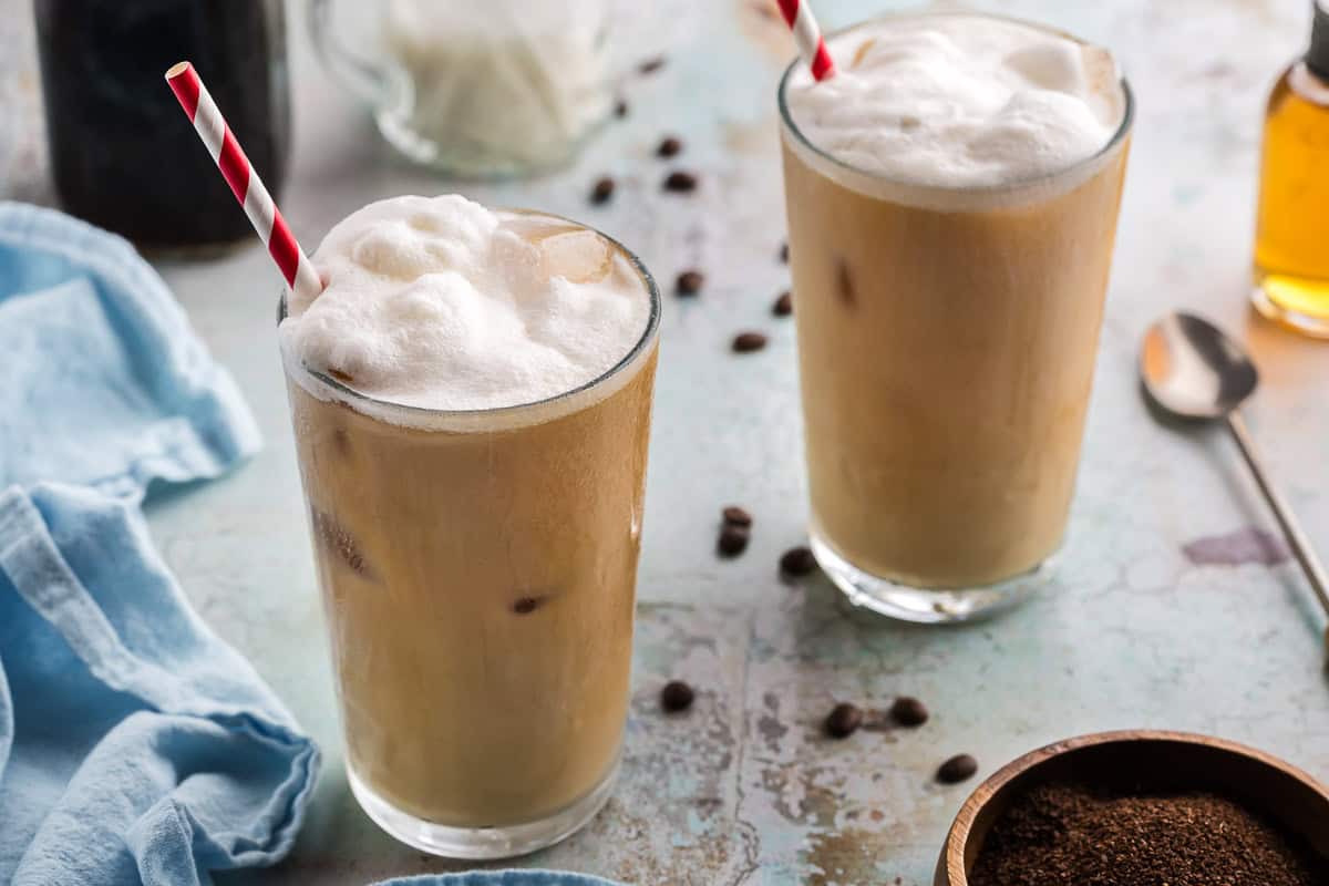 a 45 degree angle shot of two large glasses of vanilla sweet cream cold brew. The drink is a creamy brown and topped with a frothy white topping.