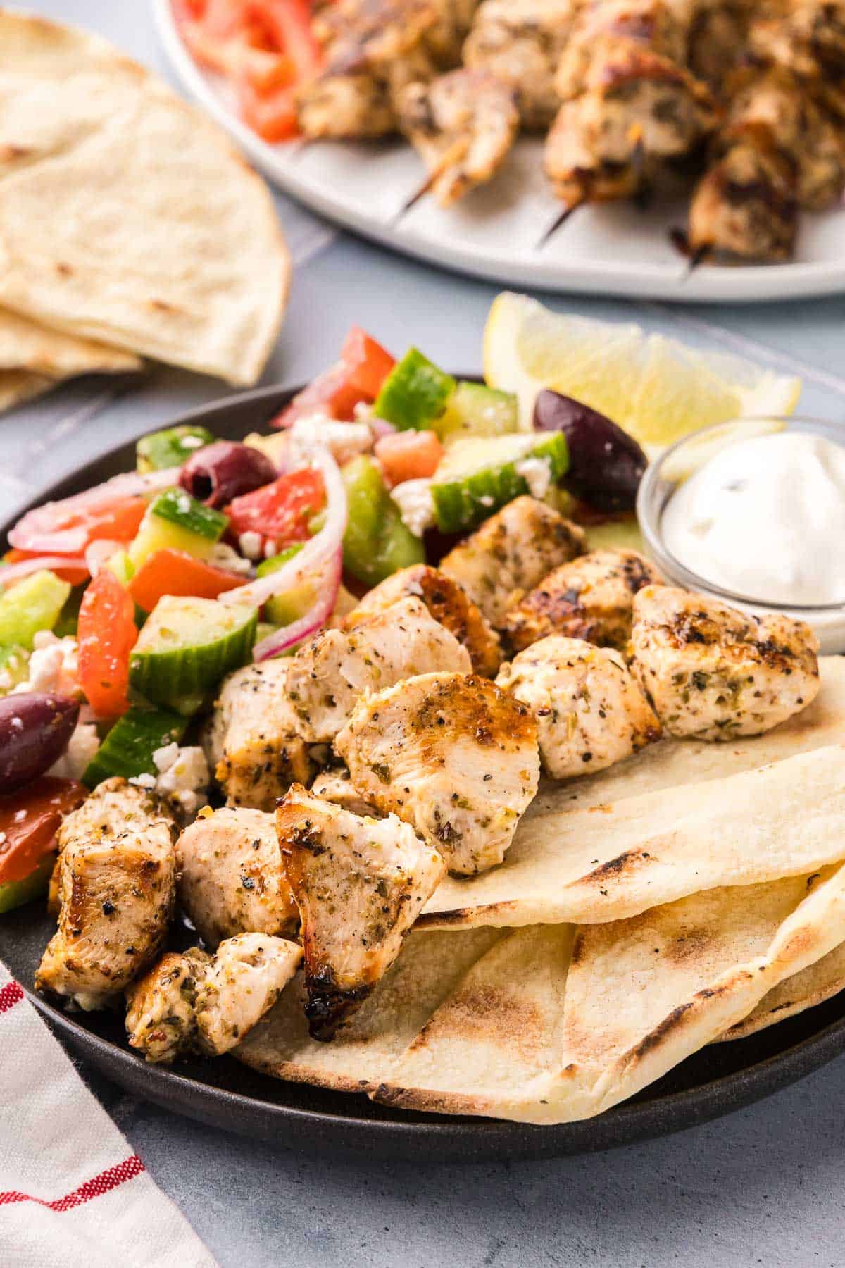 side shot of a plate filled with chicken souvlaki removed from the skewer and served alongside a Greek salad and pita bread.