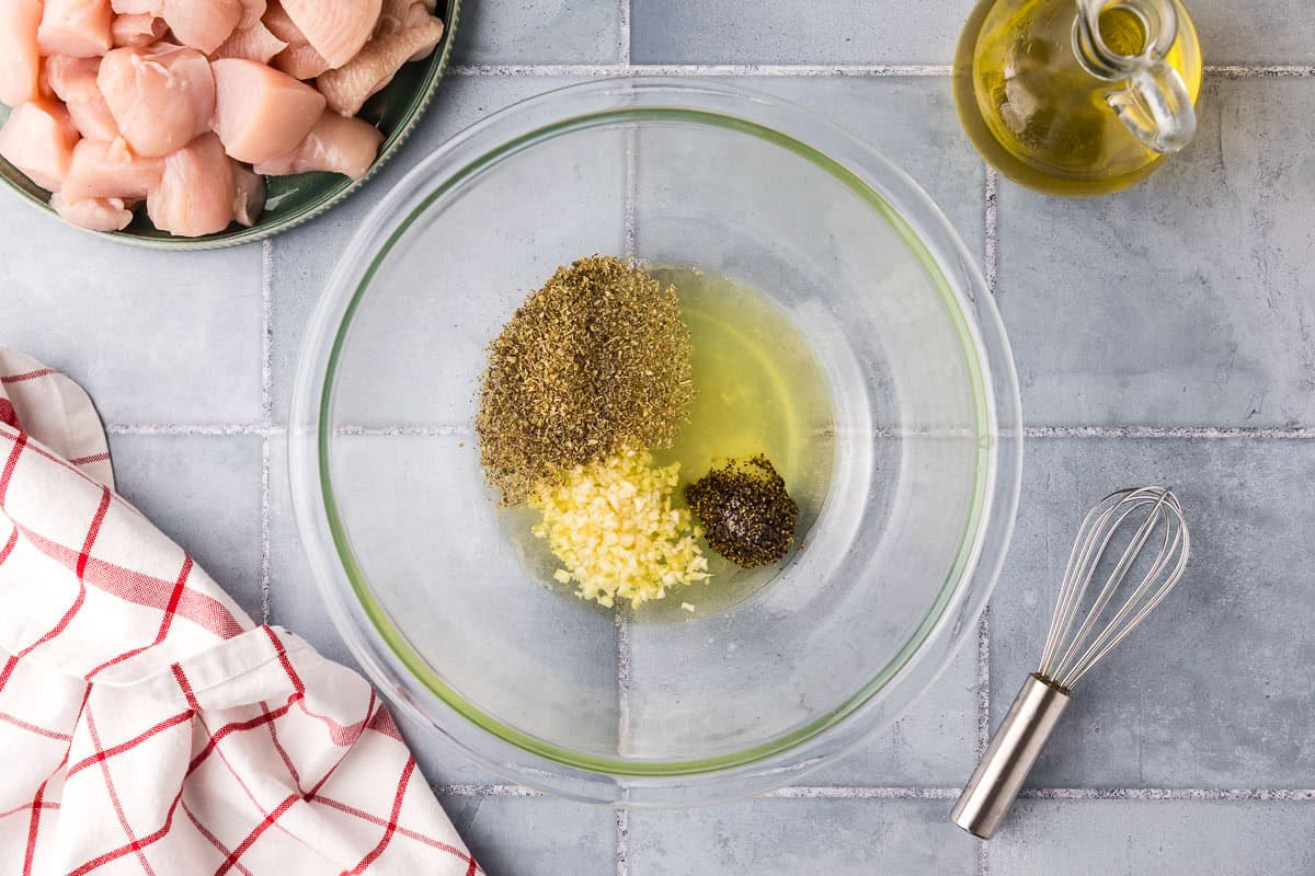 overhead shot of all the marinade ingredients added to a glass bowl. There is oil, lemon juice, salt, pepper, garlic, and dried oregano.