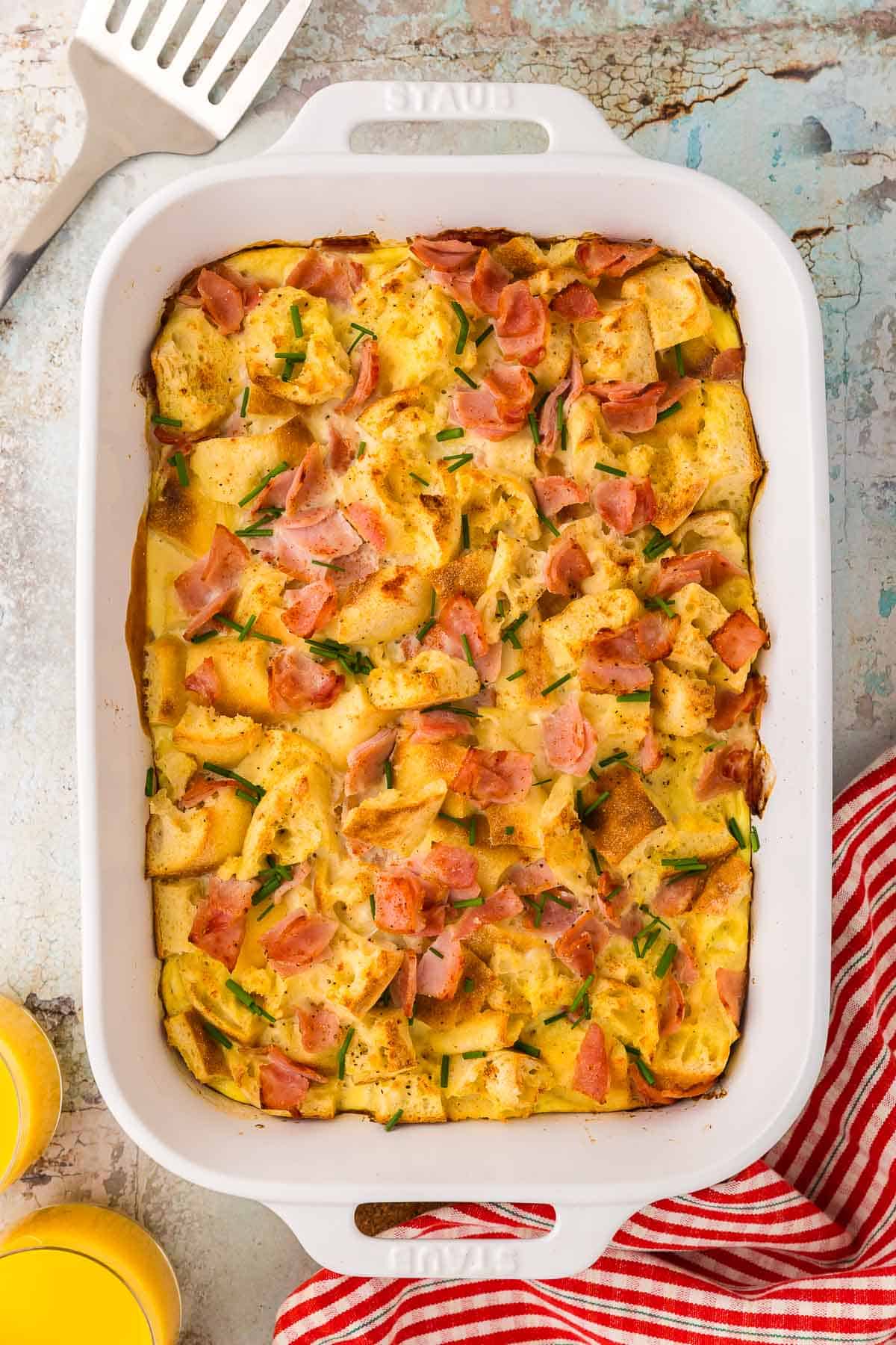 An overhead shot of the 9x13 white casserole dish filled with Eggs Benedict Casserole. It is chunky with toasted English muffin pieces, and back bacon.