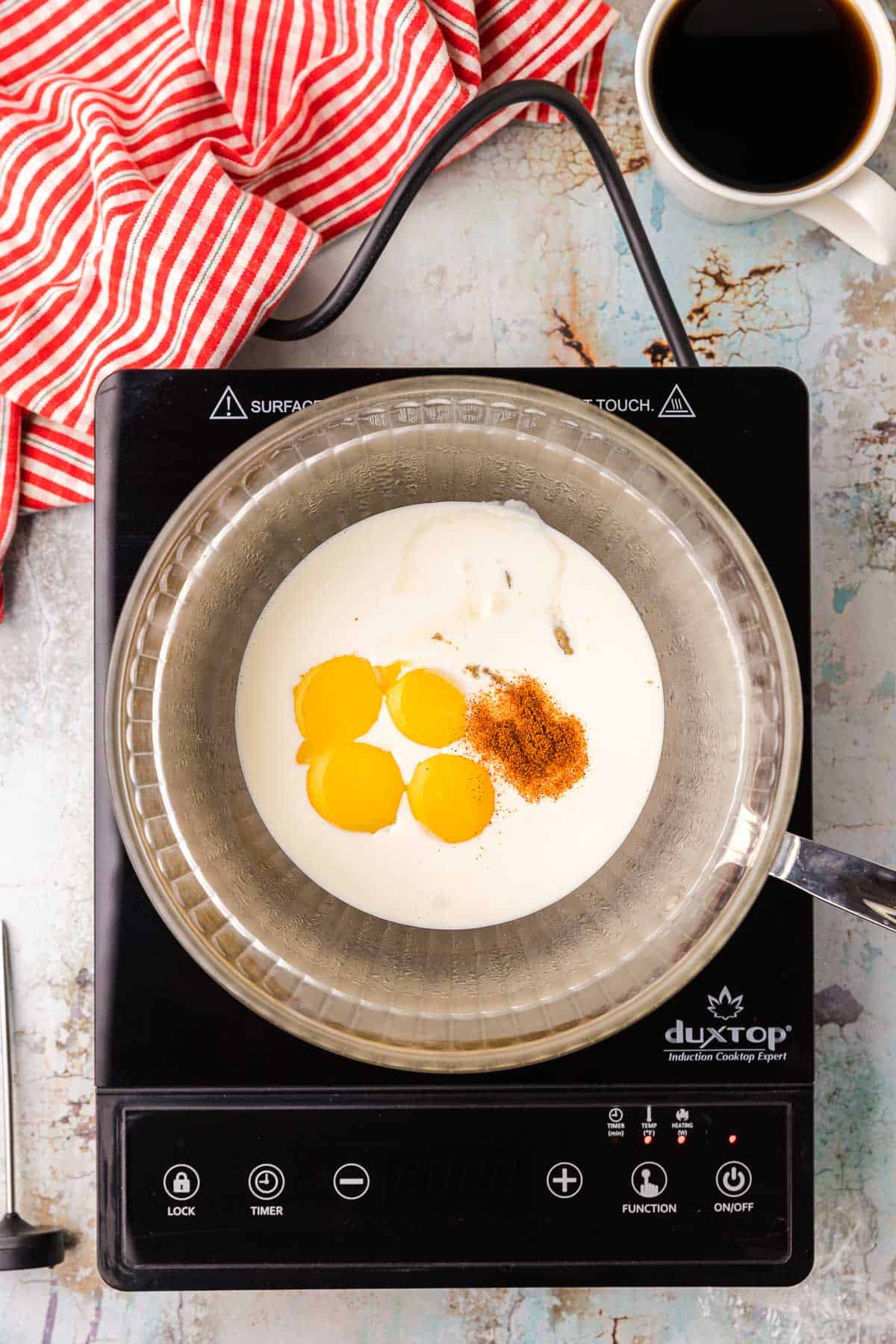A glass bowl over a double boiler is filled with heavy cream, egg yolks, lemon juice, and cayenne.