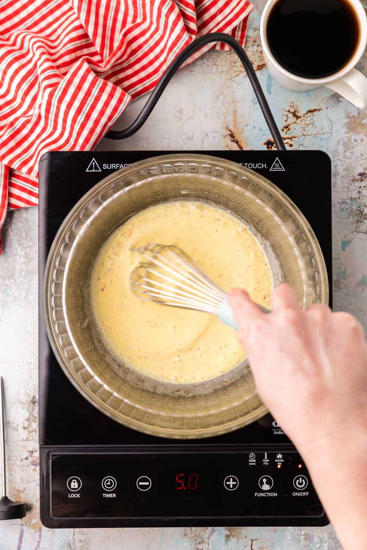 The creamy yellow Hollandaise sauce is being whisked in a glass bowl on top of a double boiler.