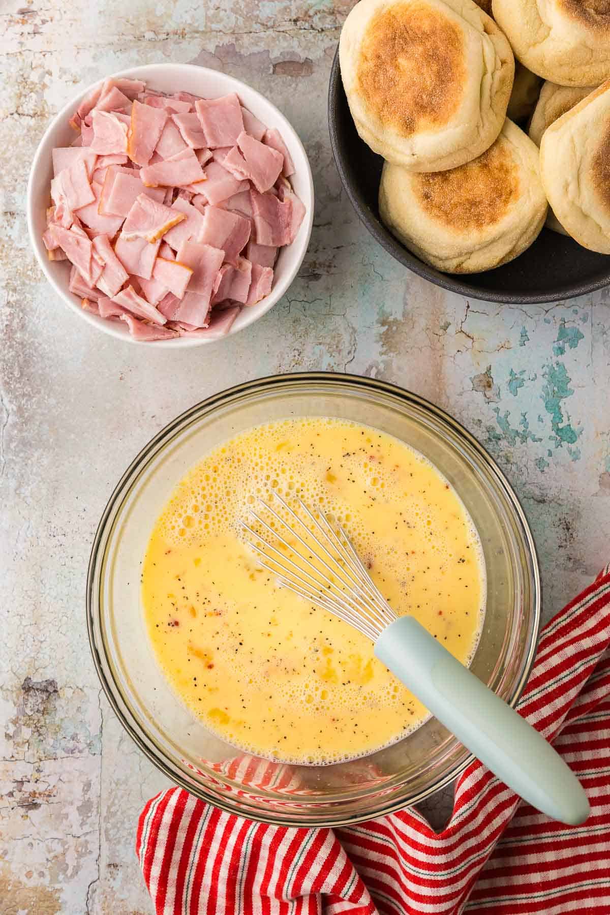 Glass mixing bowl filled with all the eggs, milk and spices to be added to the eggs benedict casserole.