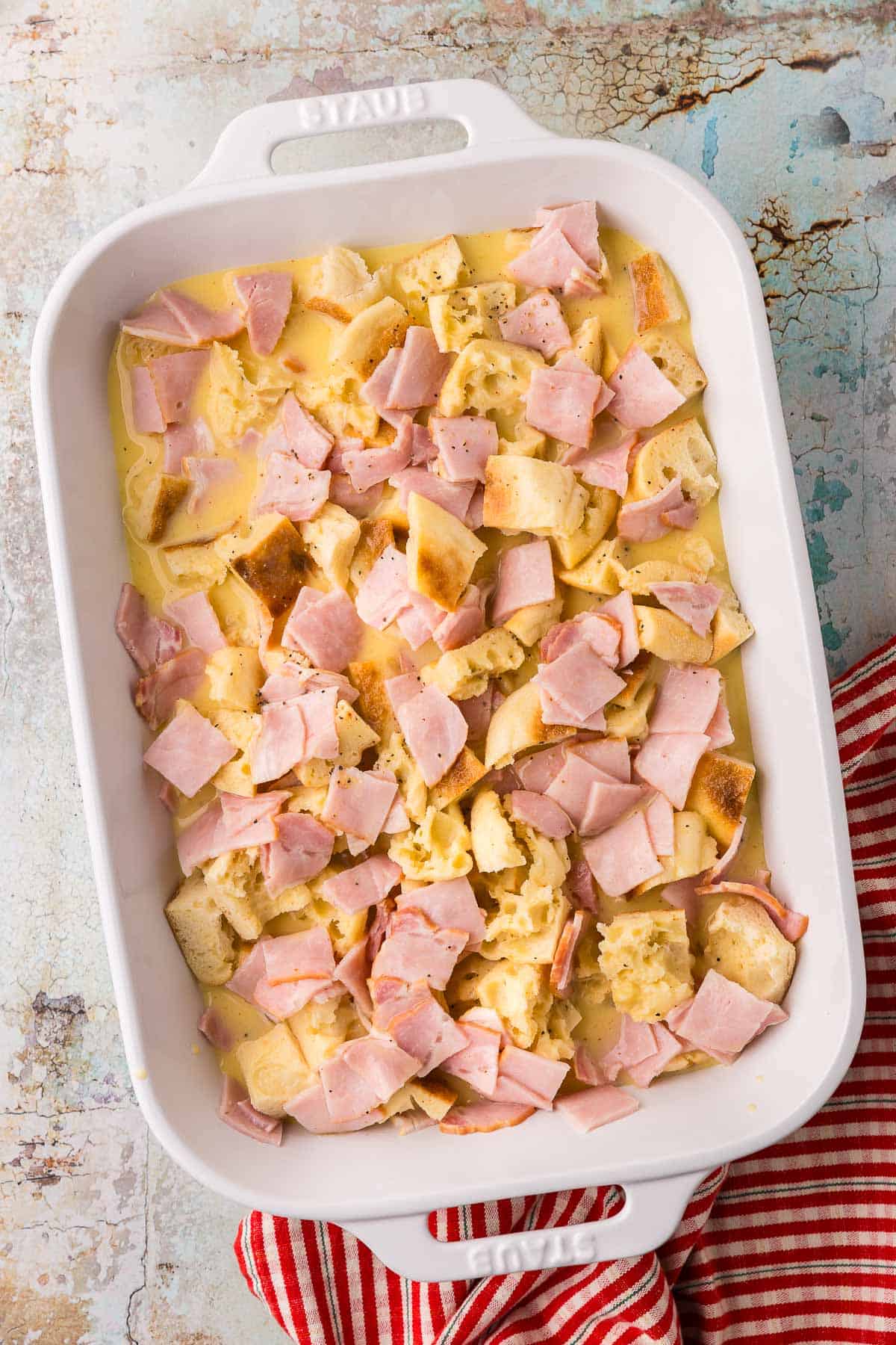 a 9x13 casserole filled with layers of back bacon, torn English muffins, and eggs. This is the assembled Eggs Benedict Casserole.