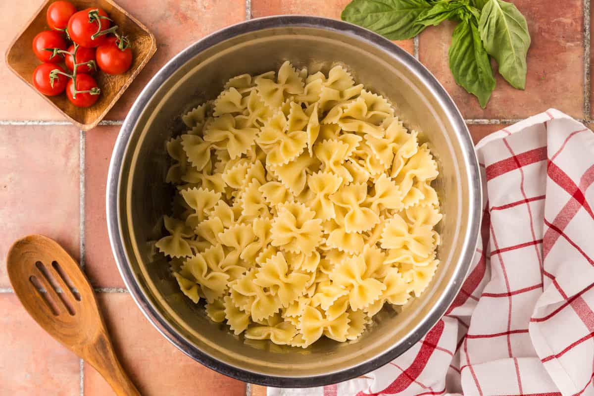Overhead shot looking into a large metal bowl filled with cooked and drained bow tie pasta.