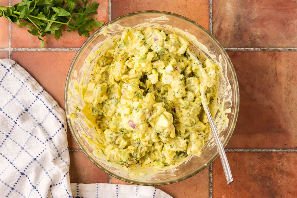 Overhead shot of a glass mixing bowl that has the cooled and boiled potatoes in it and mixed together with the dressing. It is a creamy yellow chunky potato salad.