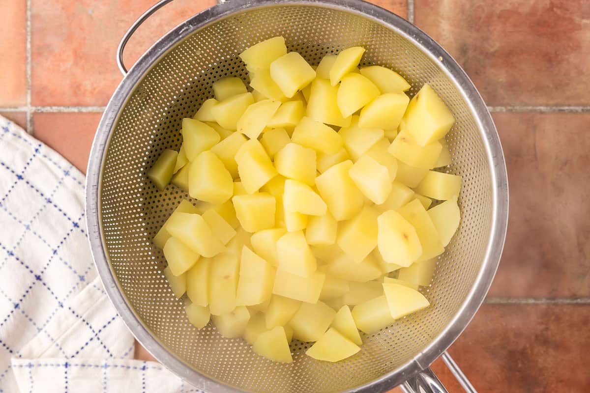 Overhead shot of potatoes being strained after they have finished boiling. The potatoes are steaming and sitting in a colander.