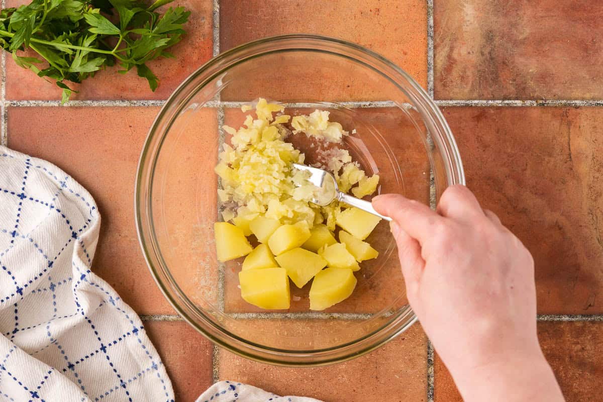 Overhead shot of a glass bowl with about ¾ cup of freshly boiled potatoes being mashed with a fork.