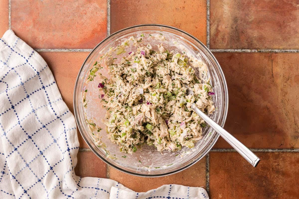 Overhead shot of a glass bowl of tuna salad. It is creamy and large chunks of veggies and tuna are apparent.