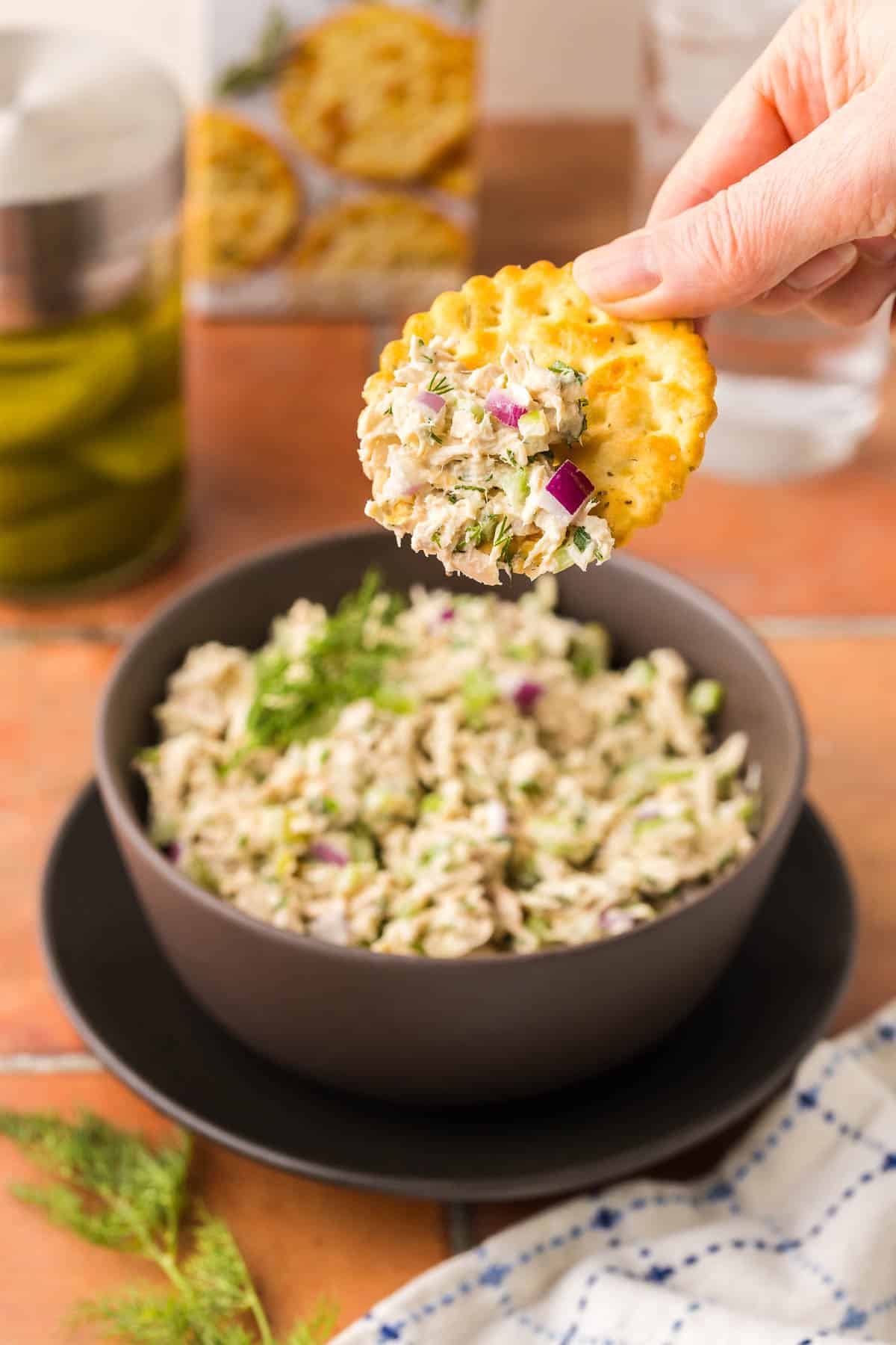 side shot of a cracker being dipped into a small bowl of tuna salad.