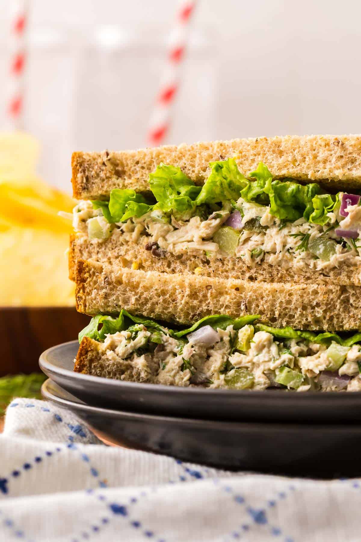 A Side shot of a sandwich stack of two cut pieces of tuna salad sandwich. Creamy and crunchy tuna salad with a leafy piece of green lettuce can be seen.