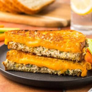 Side shot of a tuna melt cut on the diagonal and stacked on top of each other. The top is golden and crispy and the inside has melty cheese and creamy tuna salad.