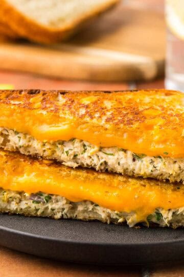 Side shot of a tuna melt cut on the diagonal and stacked on top of each other. The top is golden and crispy and the inside has melty cheese and creamy tuna salad.