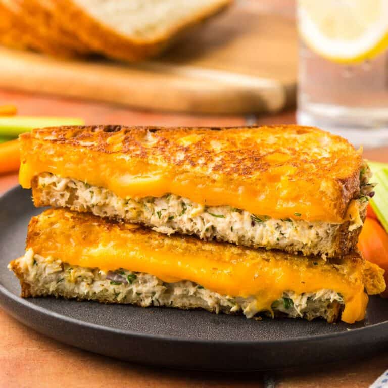 Side shot of a tuna melt cut on the diagonal and stacked on top of each other. The top is golden and crispy and the inside has melty cheese and creamy tuna salad.