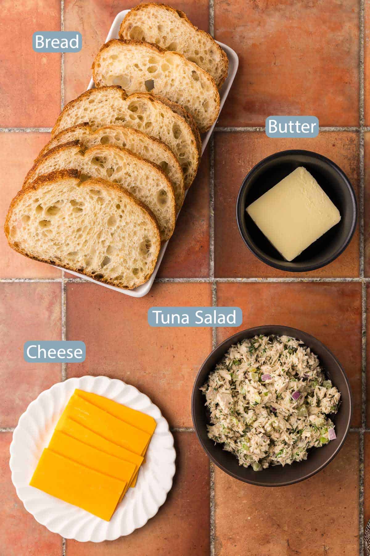 Overhead shot of the ingredients used to make a tuna melt. Ingredients are: tuna salad, butter, sliced cheese and sliced bread.
