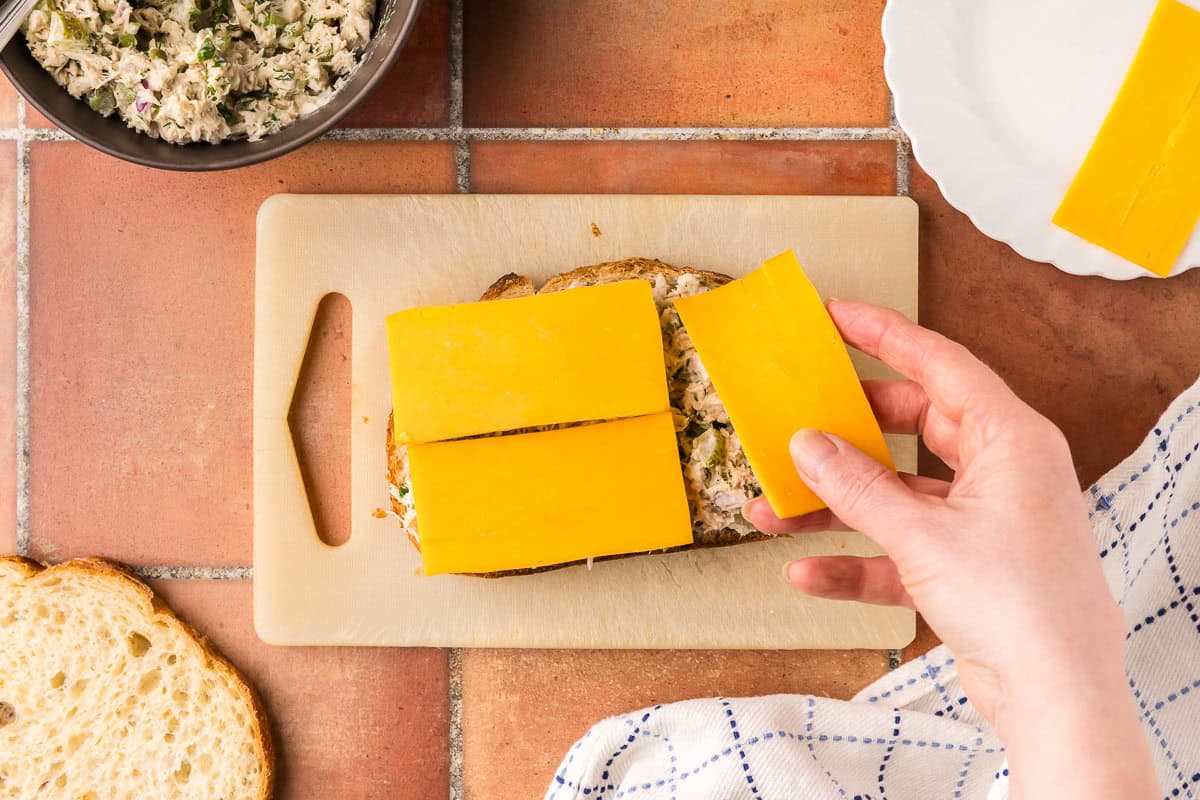 overhead shot of cheddar cheese being added to the top of an open faced tuna melt.