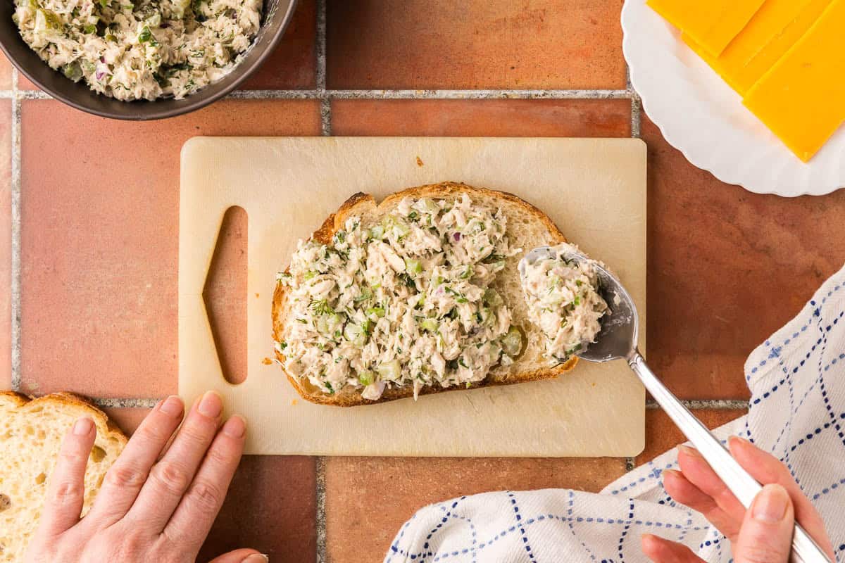 Overhead shot of tuna salad being spooned on to a slice of bread.