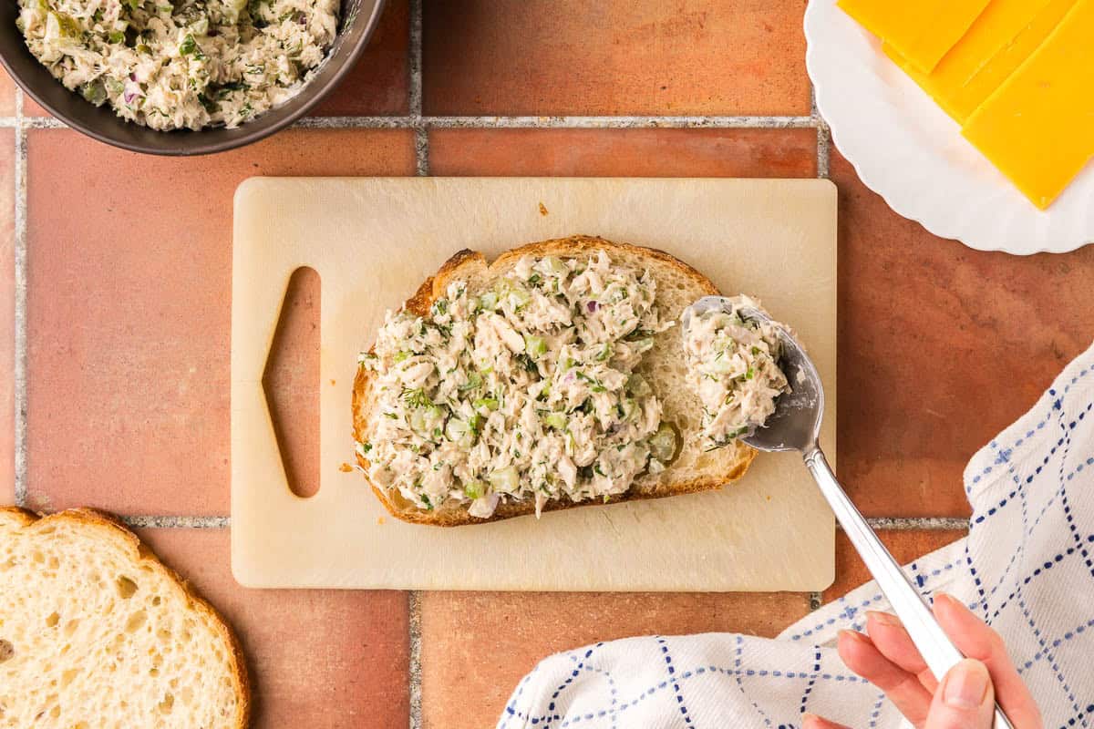 An overhead shot of tuna salad being added on top of a slice of sourdough bread.