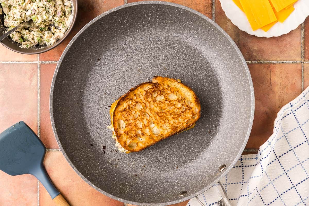 overhead shot of a non-stick pan cooking the tuna melt. The top of the tuna melt is a delicious golden brown.