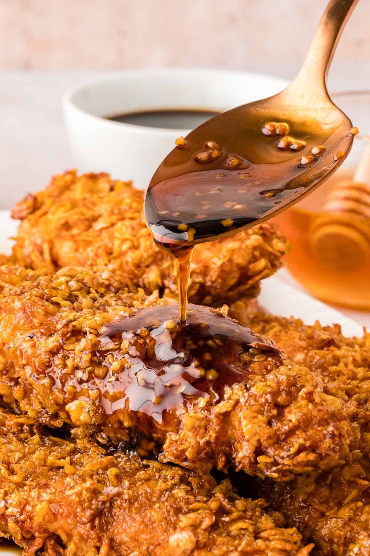 Closeup shot of chicken tenders piled on each other while a sweet sticky dark sauce is spooned over.