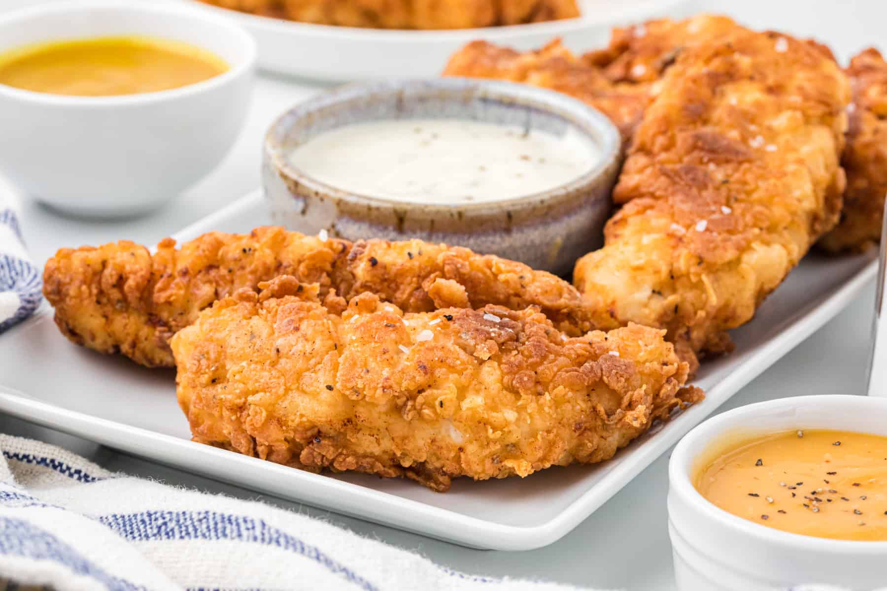 Side shot of homemade chicken tenders on a serving plate with cool ranch dressing and a honey mustard condiment as well.
