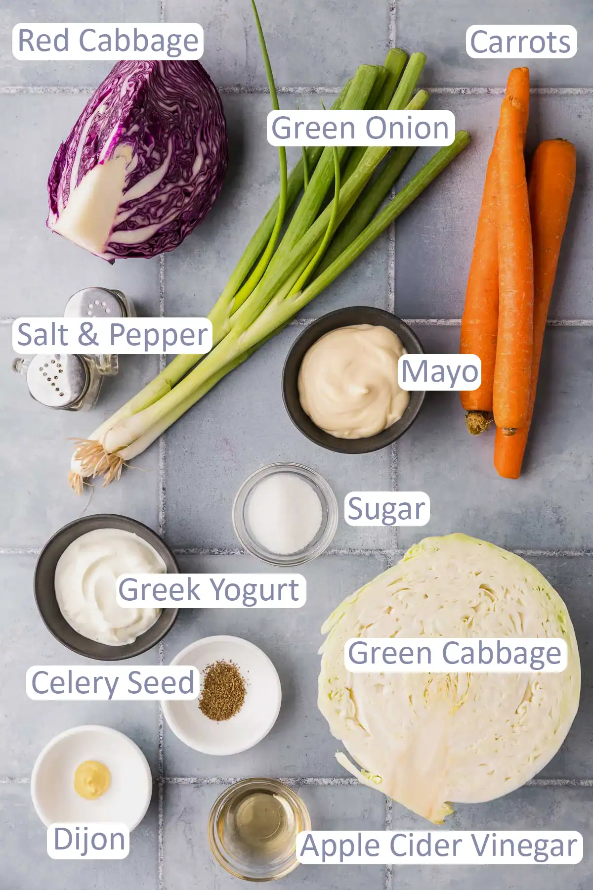 Overhead shot of all the ingredients used to make coleslaw. Ingredients are: Red and green cabbage, green onions, carrots, mayonnaise, Greek yogurt, salt and pepper, sugar, celery seed, Dijon mustard, and apple cider vinegar.