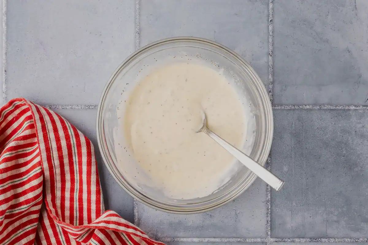 Overhead shot of a small glass bowl of white creamy coleslaw dressing.