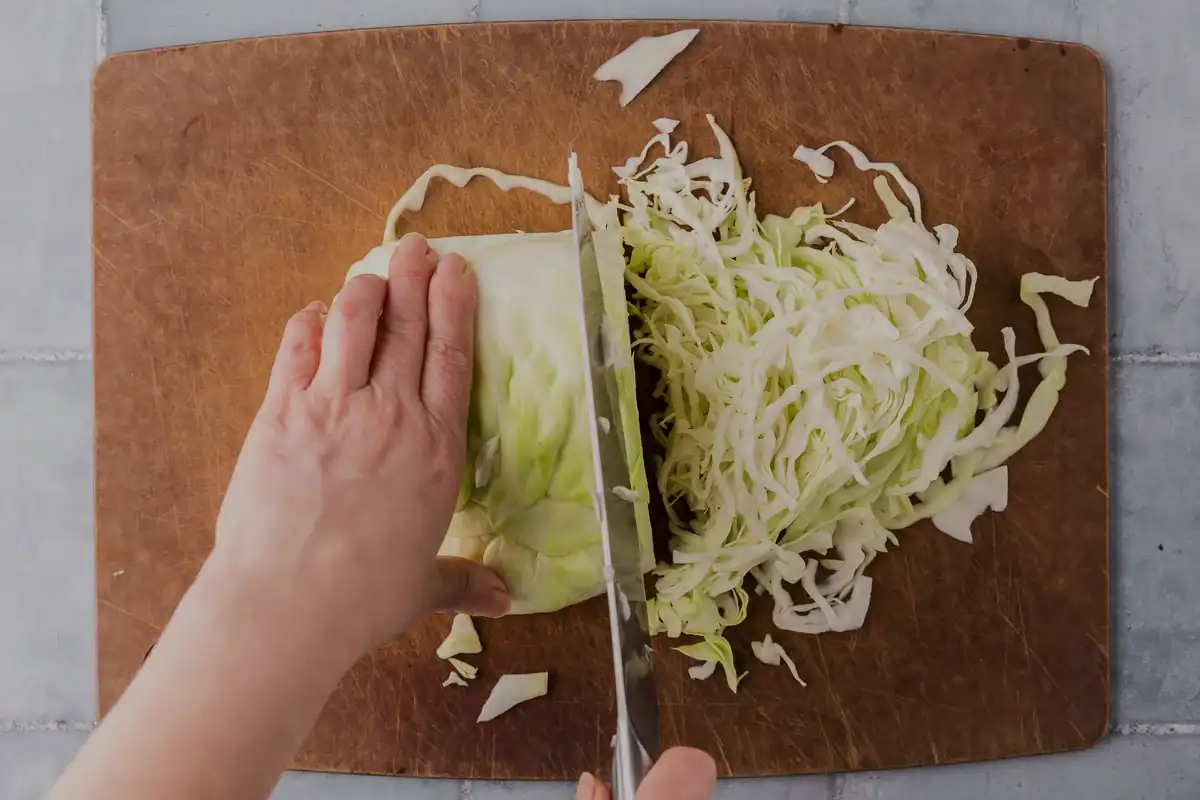 Overhead shot of a quarter head of cabbage being thinly sliced for coleslaw.