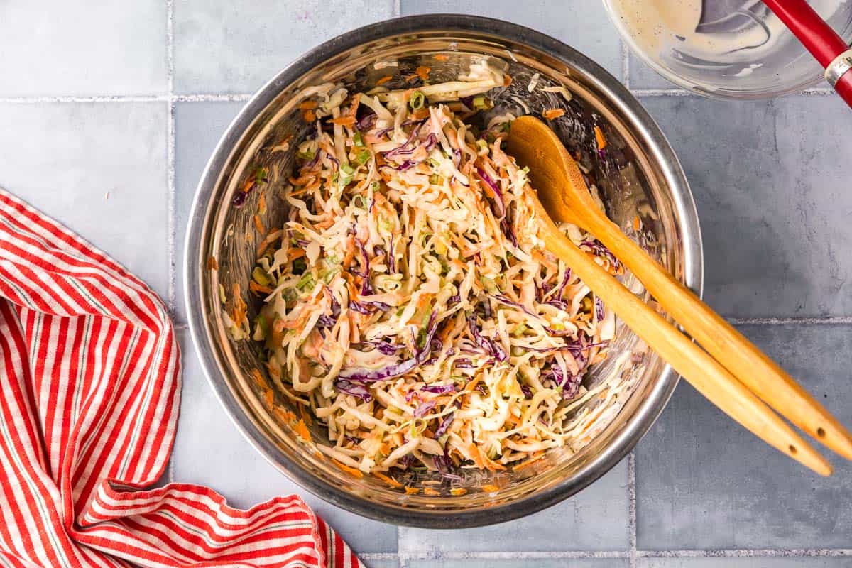 Overhead shot looking into a metal mixing bowl. All the veggies have been mixed with the dressing to make a creamy and crunchy coleslaw.