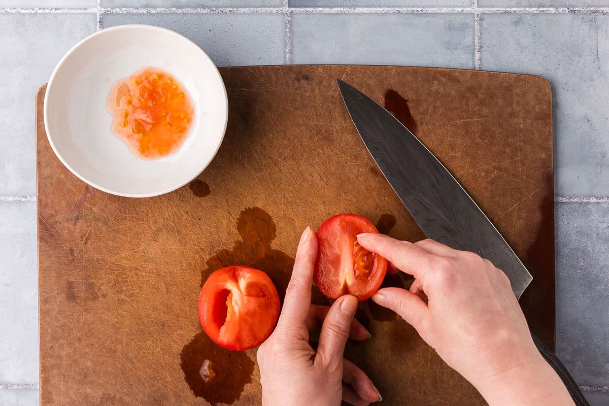 overhead shot showing a tomato sliced in half and being de-seeded.