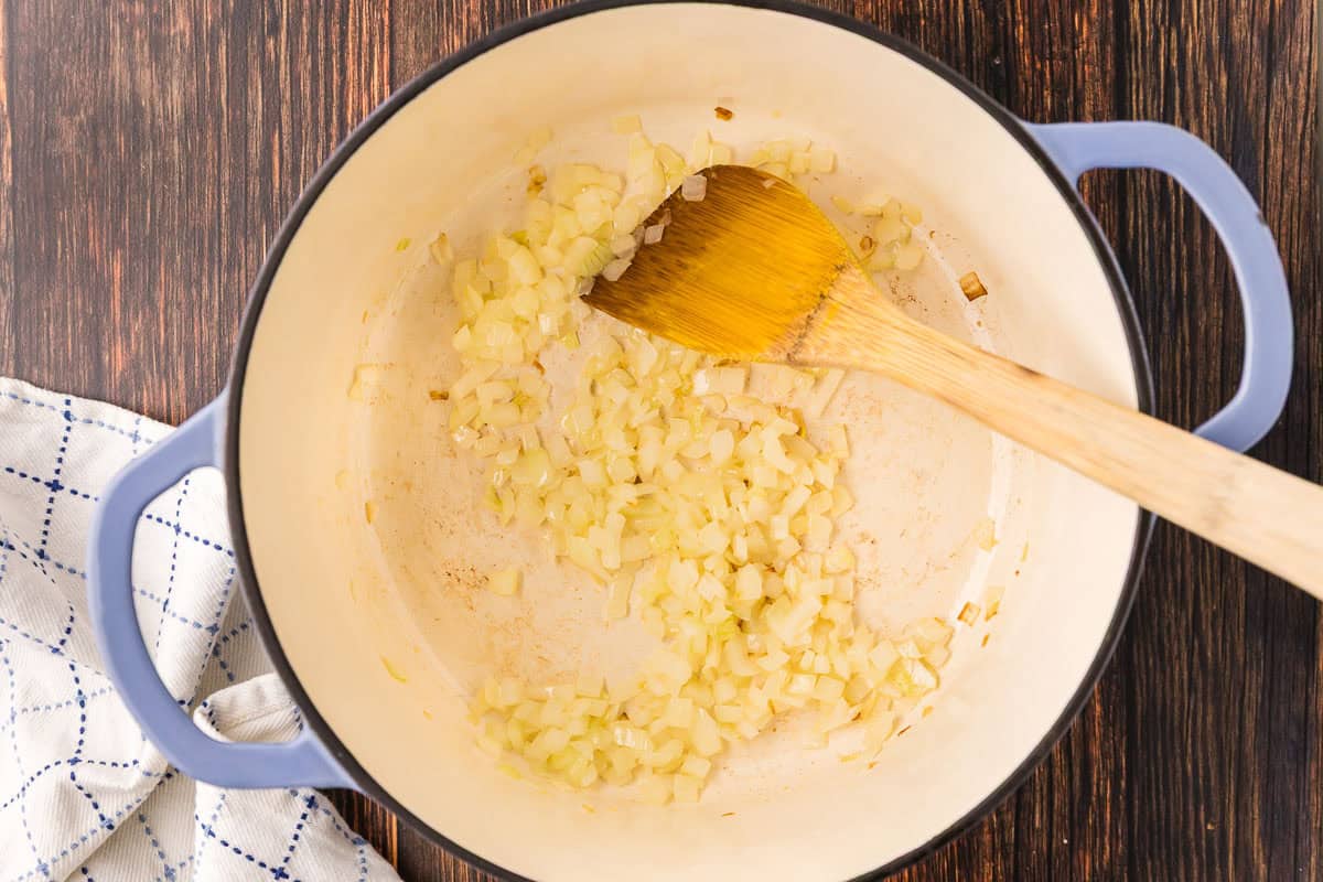 Overhead shot of a Dutch oven with diced onions sauteing inside. A wooden spatula is resting in the Dutch oven.