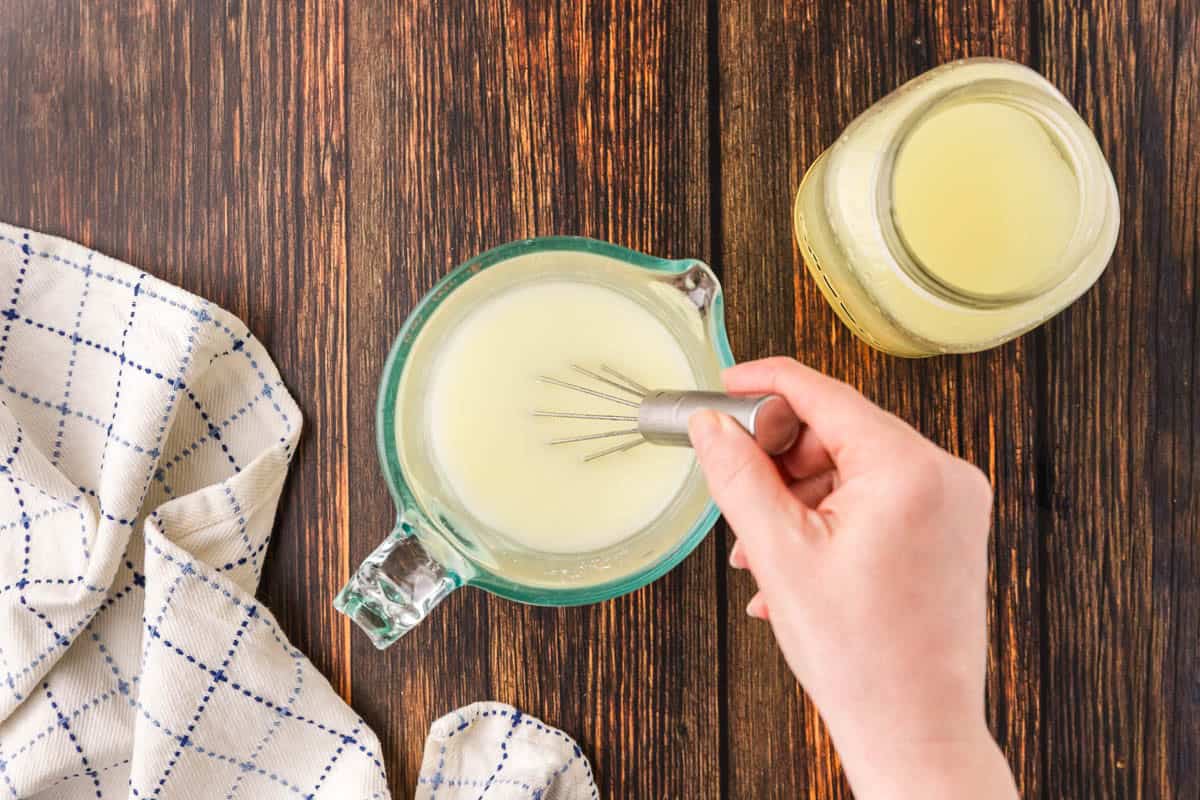 overhead shot of a measuring cup of chicken stock having cornstarch whisked in.